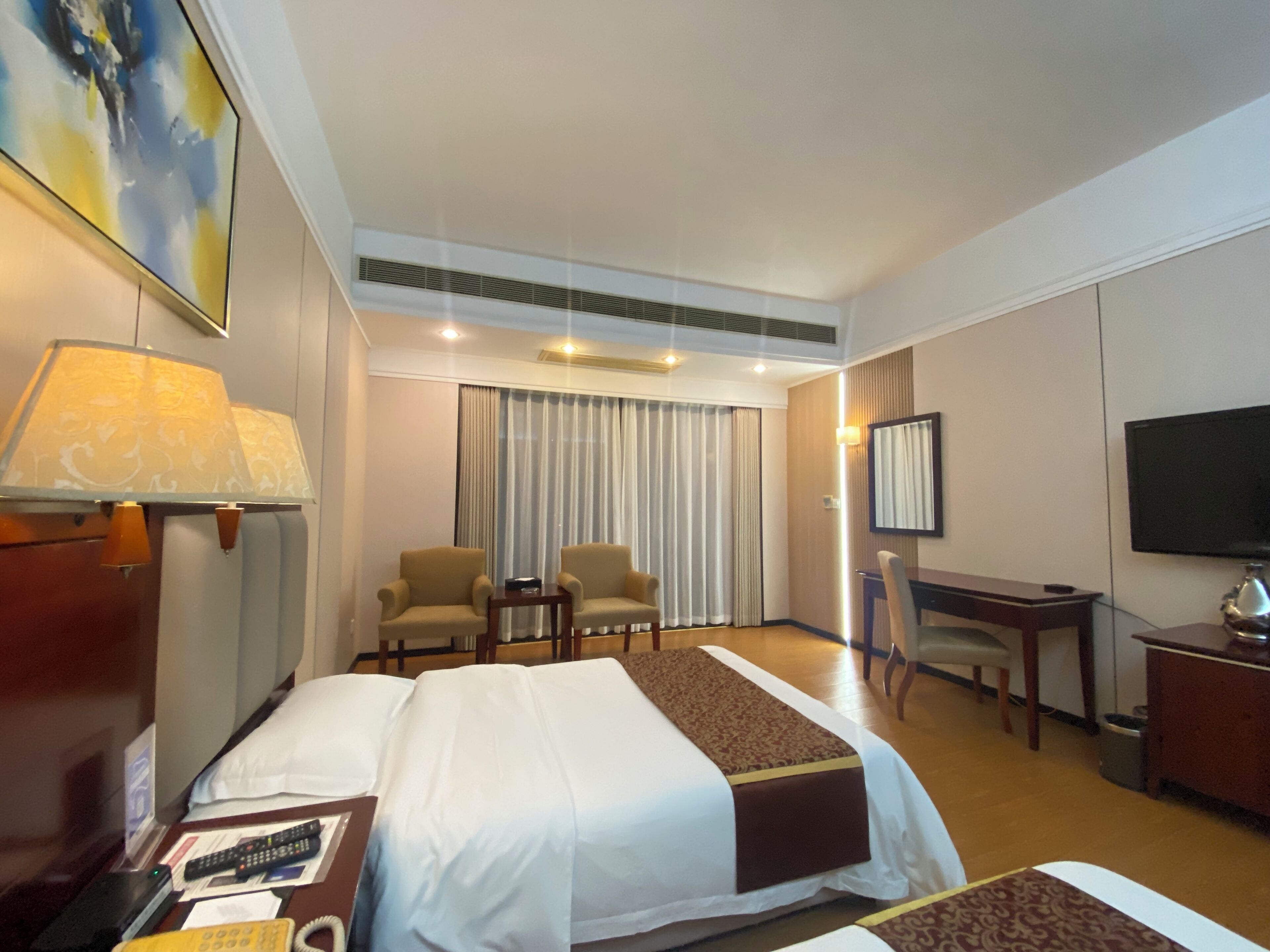 A hotel room with a large bed, two armchairs, a desk, a television, and a painting on the wall.