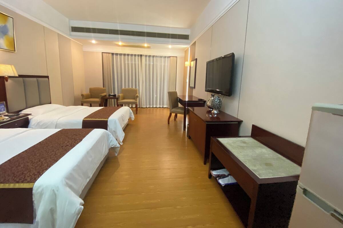 Una habitación de hotel con dos camas, un escritorio, una silla, un televisor y un ventanal con cortinas.