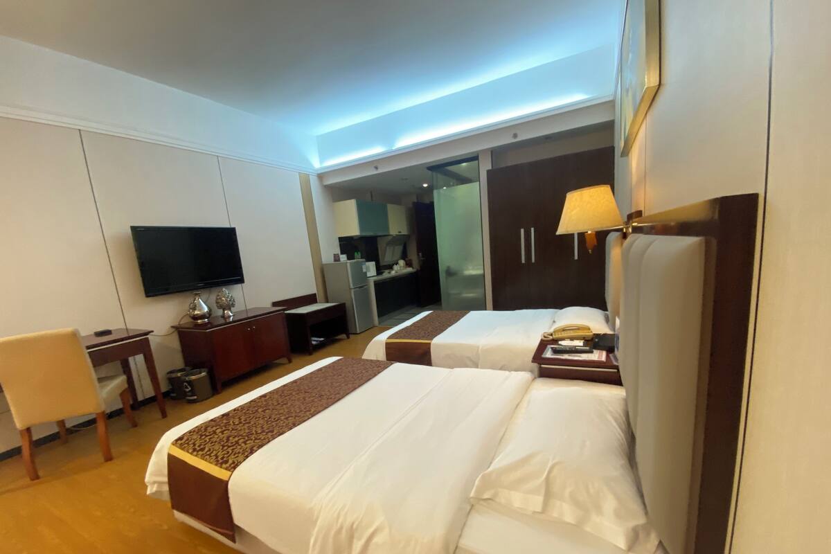 Habitación de hotel con dos camas, un escritorio, televisor, minibar y puerta corrediza al baño.