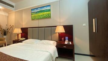 A hotel room with a large bed, two bedside tables with lamps, a nightstand with a phone and a remote control, a wardrobe, and a painting on the wall.