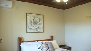Un dormitorio con cabecera de madera, un cuadro grande con motivos florales en la pared y una colcha estampada.