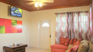 Una sala de estar con televisor, sofá, una mesita y una puerta con ventanal.