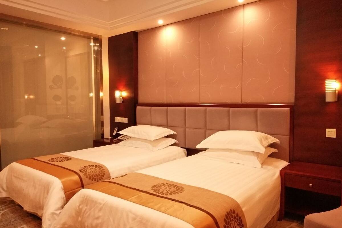 A hotel room with two beds, a large padded headboard, and a glass shower enclosure.