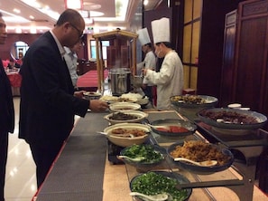 A buffet with various dishes and a man serving food.
