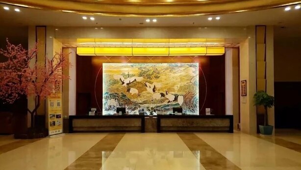 A lobby with a reception desk, a large illuminated artwork, and a polished marble floor. - Jiuhuashan Center Hotel (Chizhou)