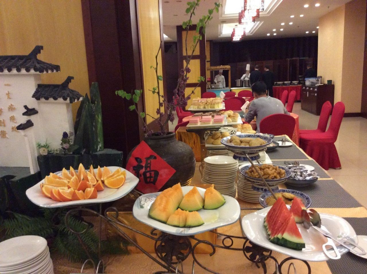 Montaje de buffet con diversos platos, entre ellos frutas y verduras cortadas, en una sala con elementos decorativos tradicionales.