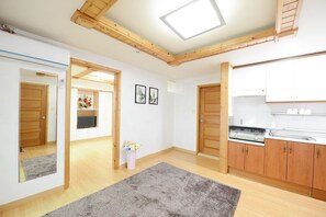 A spacious room with wooden beams, a kitchen area, and a hallway leading to another room.