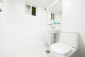 A bathroom with a white toilet, a sink, and a shower. There is a small window above the toilet and a mirror above the sink.