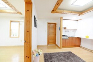 A spacious living area with wooden beams, a kitchen with wooden cabinets, and a grey rug.