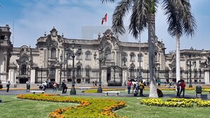 Un edificio histórico con arquitectura ornamentada, un patio central con palmeras y una bandera ondeando en la cima.