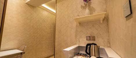 Casa de banho de hotel com lavatório branco, espelho, prateleira com artigos de higiene e uma orquídea pendurada.
