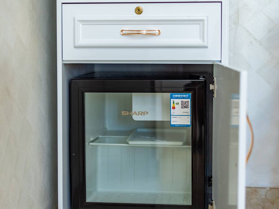 A compact kitchen with a built-in refrigerator, a kettle, and a microwave on a countertop.