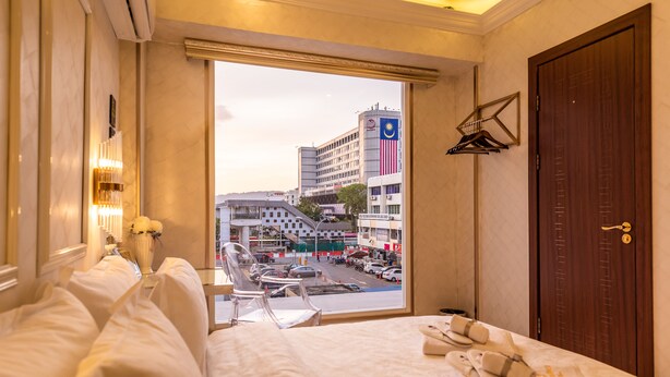 Habitación de hotel con cama, ventana con vista a la ciudad, puerta de madera y perchero en la pared.