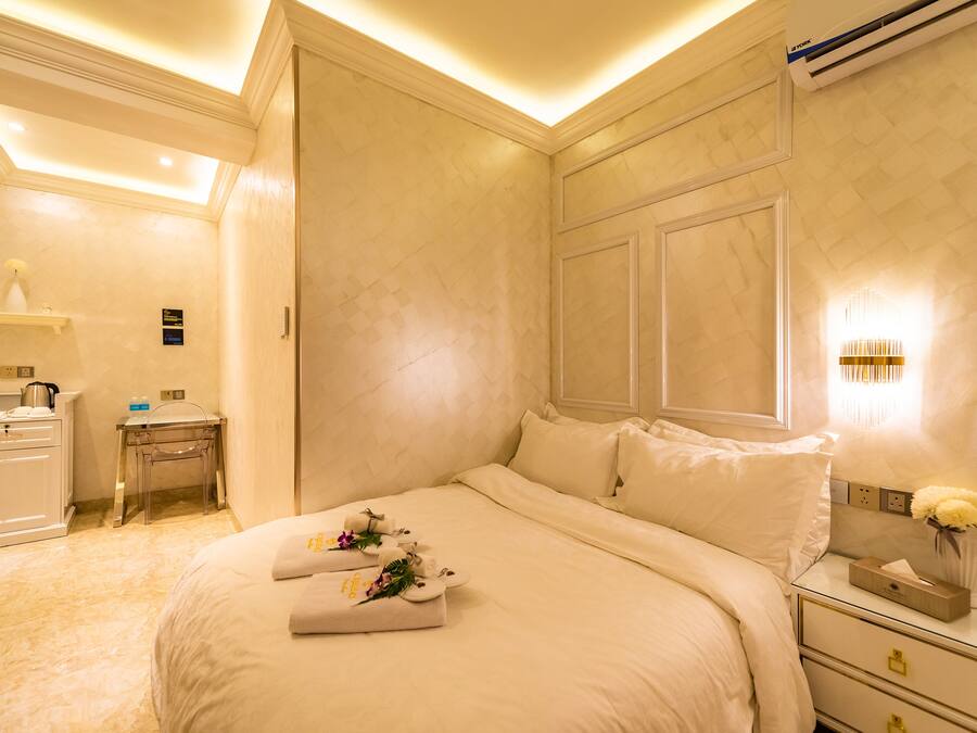 Una habitación de hotel con una cama grande, un escritorio y una mesita de noche con un jarrón de flores.