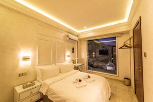 Ein Hotelzimmer mit einem großen Bett, Nachttischen, einem Fenster mit Blick auf die Stadt und einer Klimaanlage.
