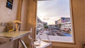 Habitación de hotel con un ventanal grande, vistas despejadas del paisaje urbano, un florero con flores y una mesa con un menú.