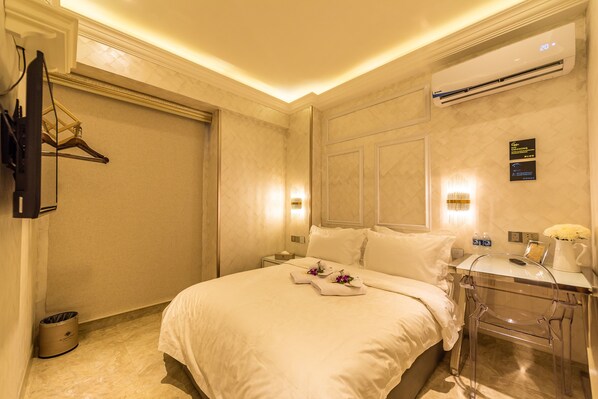 A hotel room with a bed, bedside table, air conditioning unit, and a wall-mounted TV.