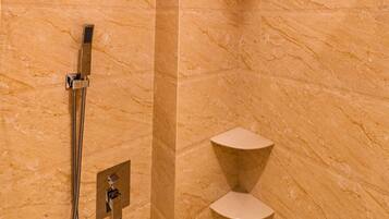 A marble-walled shower with a handheld showerhead and a fixed overhead showerhead.