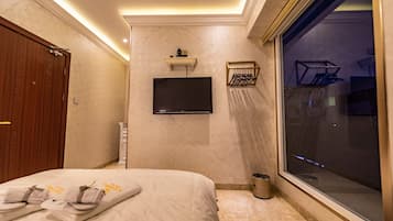 A hotel room with a bed, a TV mounted on the wall, a window, and a door.