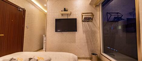 A hotel room with a bed, a TV mounted on the wall, a window, and a door.