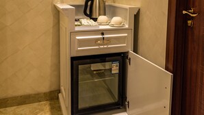 Un minibar compacto con cafetera, una copa y un florero con flores.