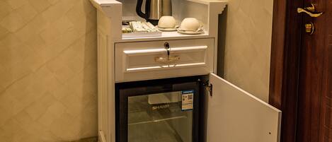 Un minibar compacto con cafetera, una copa y un florero con flores.