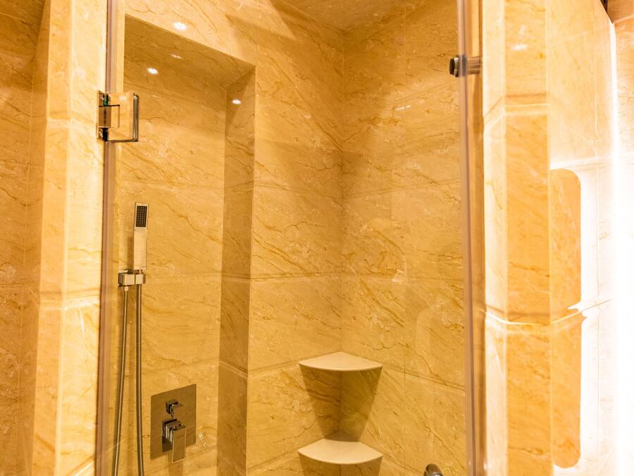 A glass-enclosed shower with a handheld showerhead and a handheld shower attachment.
