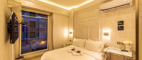 Habitación de hotel con cama, escritorio con silla, televisor montado en la pared y ventana con vistas a edificios.