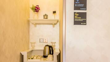 A compact kitchenette with a coffee maker, a kettle, and a small shelf with decorative items. There are signs indicating WiFi availability and a no-smoking policy.