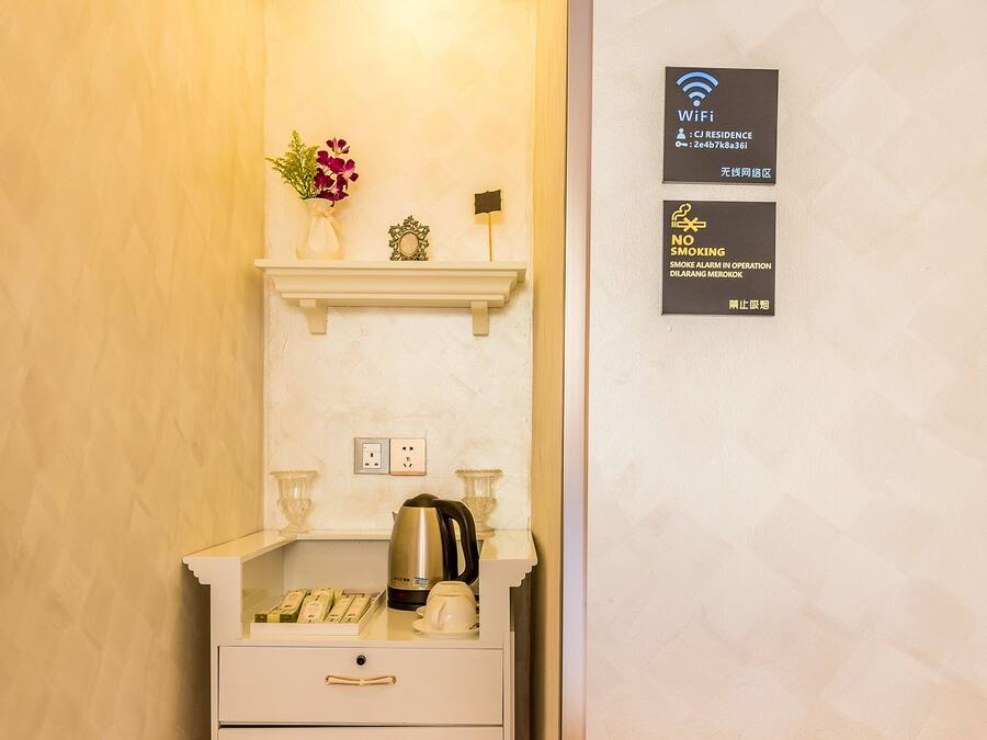 A compact kitchenette with a coffee maker, a kettle, and a small shelf with decorative items. There are signs indicating WiFi availability and a no-smoking policy.