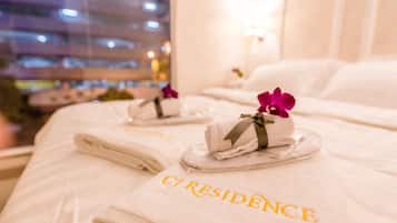 A hotel room with neatly folded towels on the bed, a visible bed number, and a window with a cityscape view.