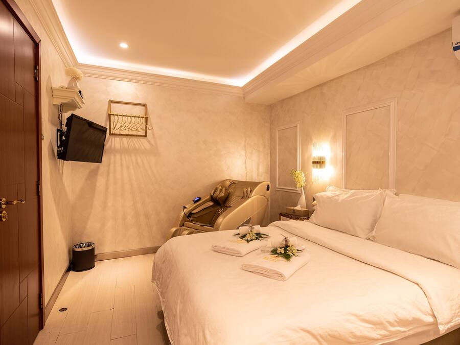Een hotelkamer met een bed, een stoel, een aan de muur bevestigde televisie en een tafeltje met een bloemenvaas.
