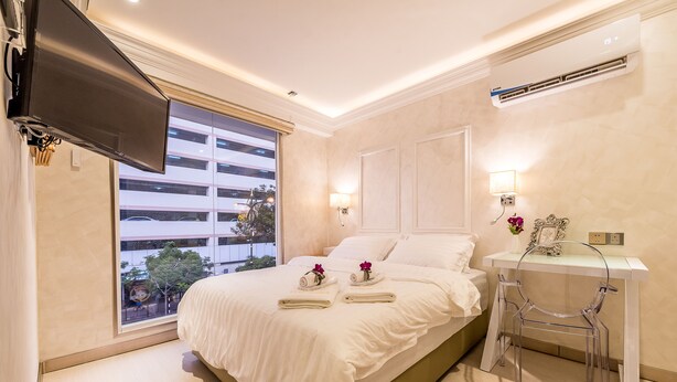 Ein modernes Hotelzimmer mit einem großen Bett, einem an der Wand montierten Fernseher, einem Schreibtisch mit Stuhl und einem Fenster mit Blick auf Gebäude.