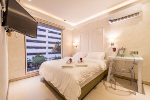 A modern hotel room with a large bed, a TV mounted on the wall, a desk with a chair, and a window with a view of buildings. - CJ Residence (Kota Kinabalu)