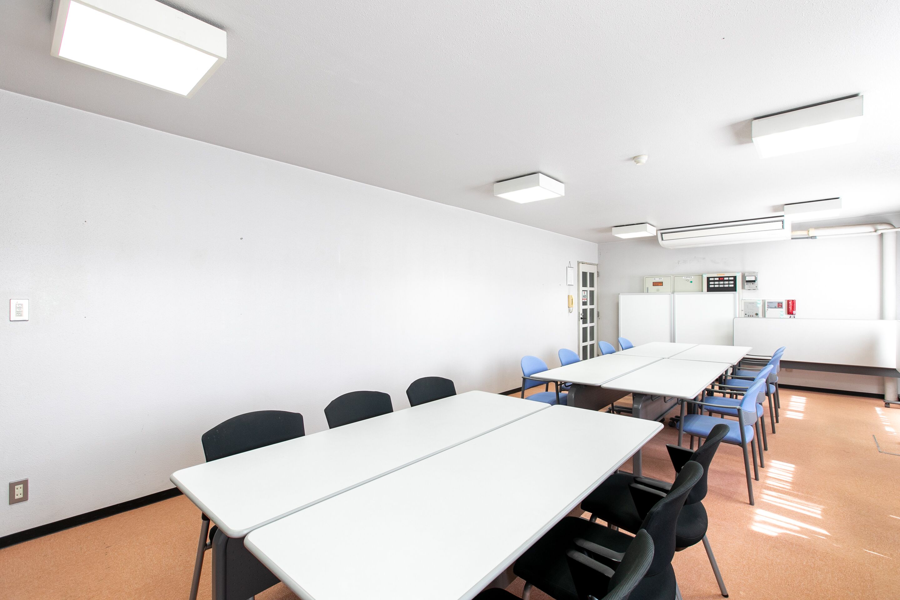 A conference room with white tables and chairs, a whiteboard, and a fire extinguisher on the wall.