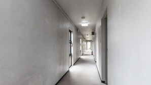 Pitkä, kapea käytävä, jonka molemmilla puolilla on ovia, oikealla puolella palosammutin ja katossa valaisin.