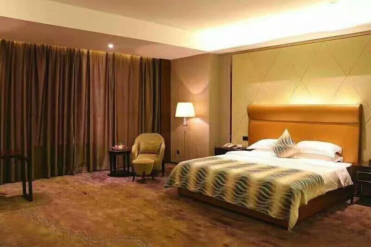 Una habitación de hotel con una cama grande, una silla, una mesita de noche, una lámpara y una cortina.