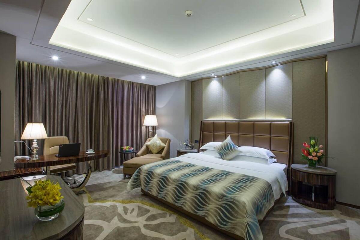 Una habitación de hotel moderna con una cama grande, un escritorio, una silla y una mesita de noche con lámpara.