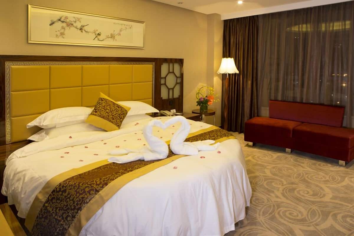 Habitación de hotel con una cama grande, un sofá rojo, una obra de arte enmarcada en la pared y una ventana con cortinas.