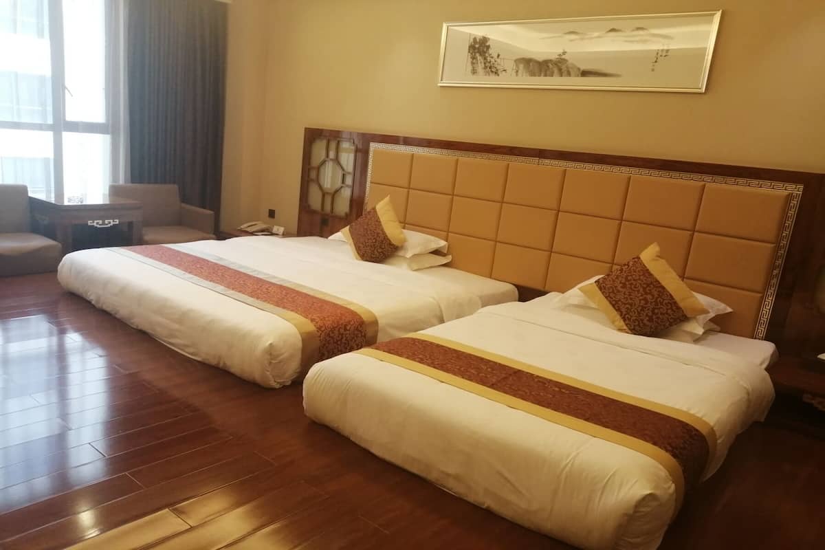 Una habitación de hotel con dos camas, piso de madera, escritorio y una silla.