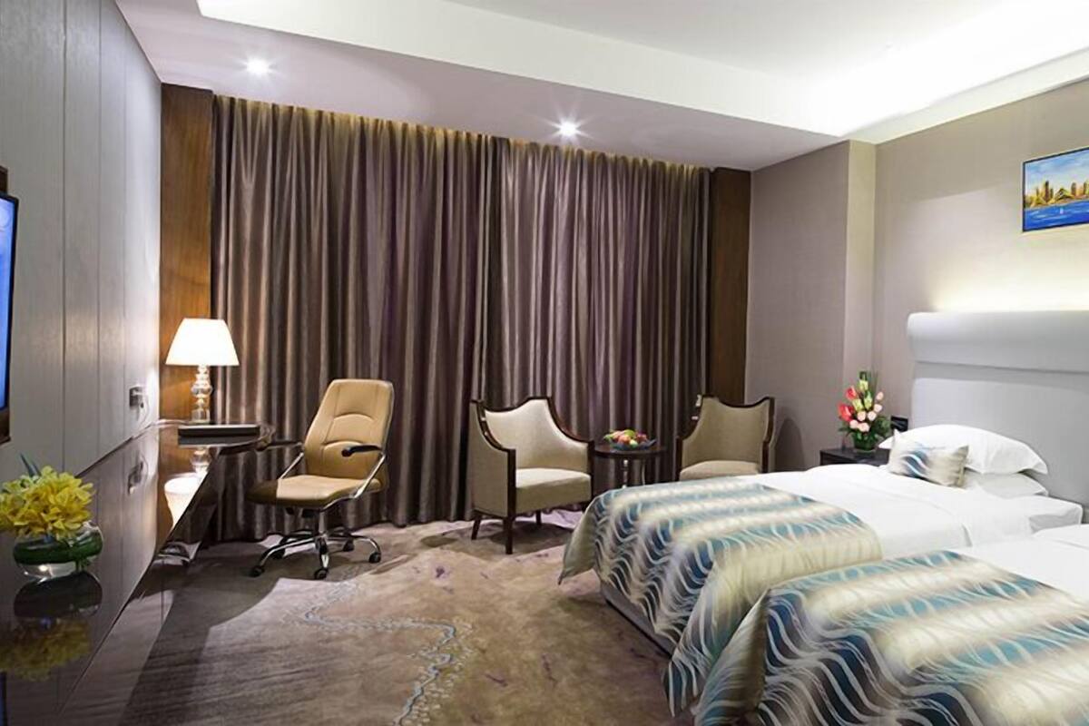 Habitación de hotel con una cama grande, dos sillones, un escritorio con lámpara, televisión y un cuadro en la pared.
