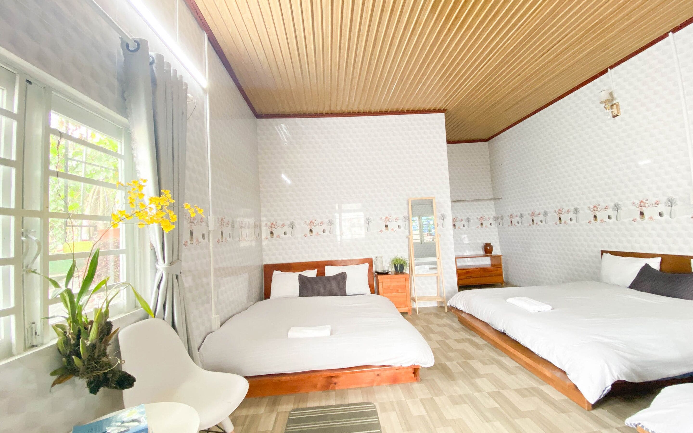 Habitación de hotel con dos camas, techo de madera y ventana con cortinas.