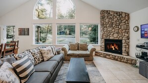 A living room with a stone fireplace, large windows, a sofa, and a coffee table. - Mt Baker Lodging's Cabin #1 - With Wifi, Hot Tub, Pet Friendly (Deming)