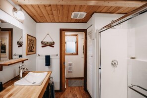 A bathroom with a wooden ceiling, a white sink, a mirror, and a shower area. - Snowline Cabin #4 - Pet-friendly Cedar Cabin With a Private Outdoor hot Tub! (Deming)