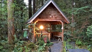 A wooden cabin with a porch, surrounded by dense forest. - Snowline Cabin #4 - Pet-friendly Cedar Cabin With a Private Outdoor hot Tub! (Deming)