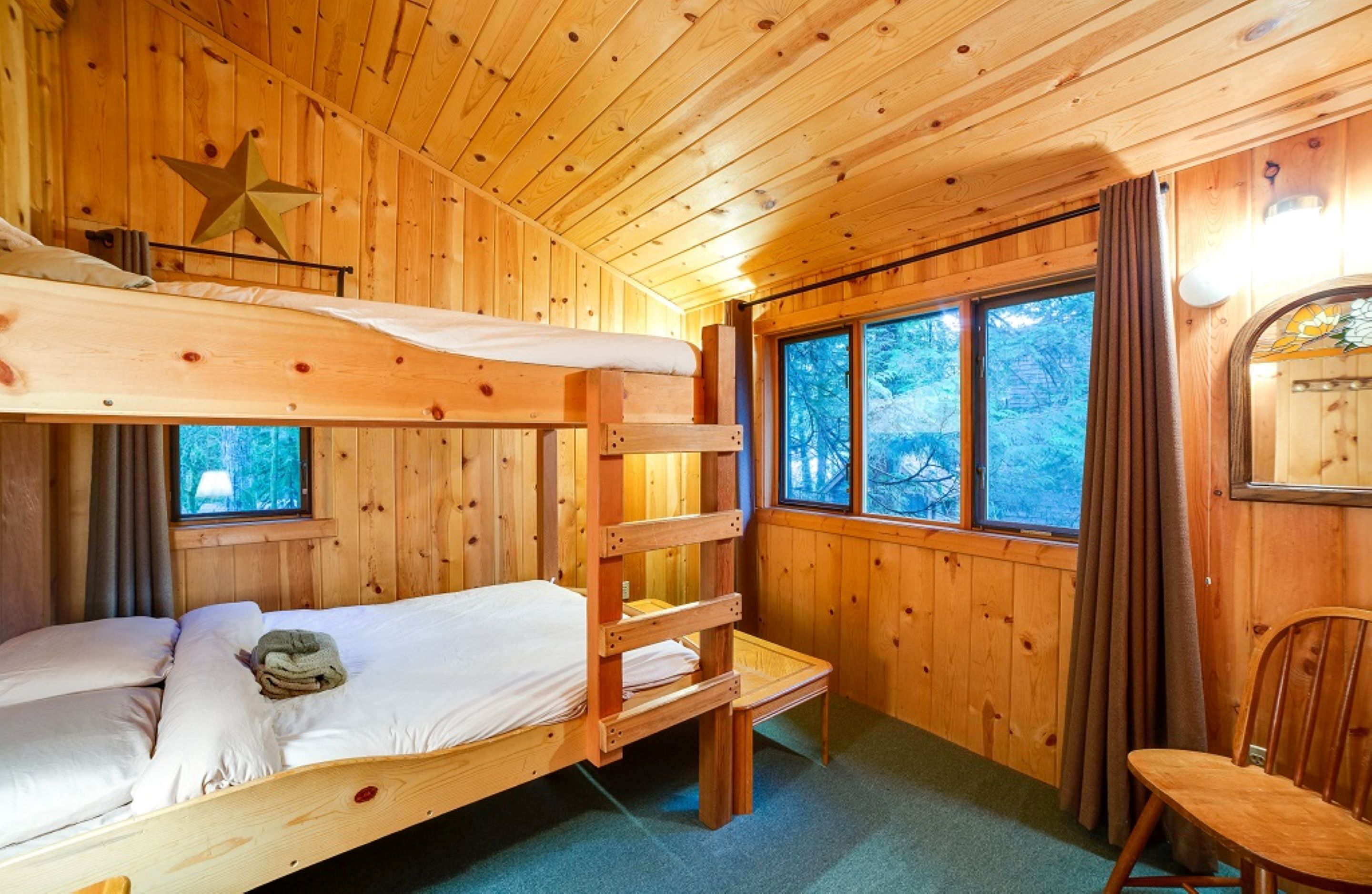 A wooden cabin room with bunk beds, a small table, and a chair.