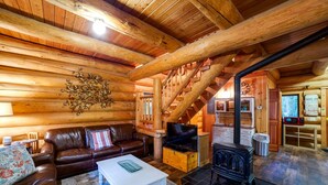 A log cabin interior with a wooden staircase, a fireplace, a leather sofa, and a television. - Snowline Cabin 10 - Log Cabin at its Best Free Wi-fi (Deming)