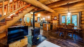 A log cabin interior with a wooden staircase, a central fireplace, a kitchen area, and a dining space. - Snowline Cabin 10 - Log Cabin at its Best Free Wi-fi (Deming)