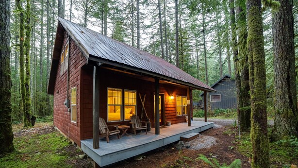 Een rustieke hut met een veranda, houten terras en grote ramen.
