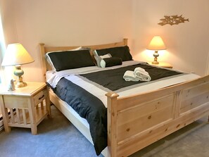 Un letto di legno con copriletto bianco e nero, due cuscini e due asciugamani piegati. Su entrambi i lati del letto, due comodini con lampade.